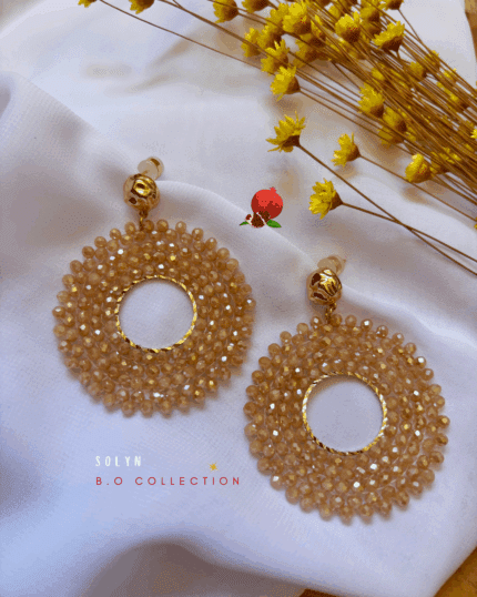 Clou d’oreille en plaqué or Pendentif tissé à la main avec perles en crystal de verre (diamètre 5 cm) 3 coloris disponibles : ambre, orange, rose/rosse fuschia Longueur : 6 cm