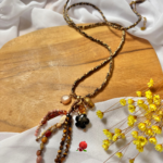 Sautoir bohème en fil tressé avec pendentifs divers en résine, acier inoxydable et breloques en pierre naturelle Pierre : tourmaline noire, rhodochrosite et oeil de tigre Longueur chaine : 88cm (+ 5cm chainette d'extension)